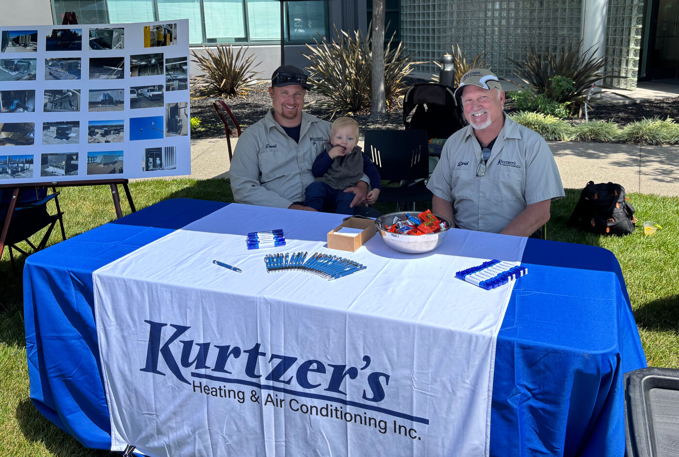 David Kurtzer and family at a community event booth with a Kurtzer's Heating & Air Conditioning table and a display board of completed jobs